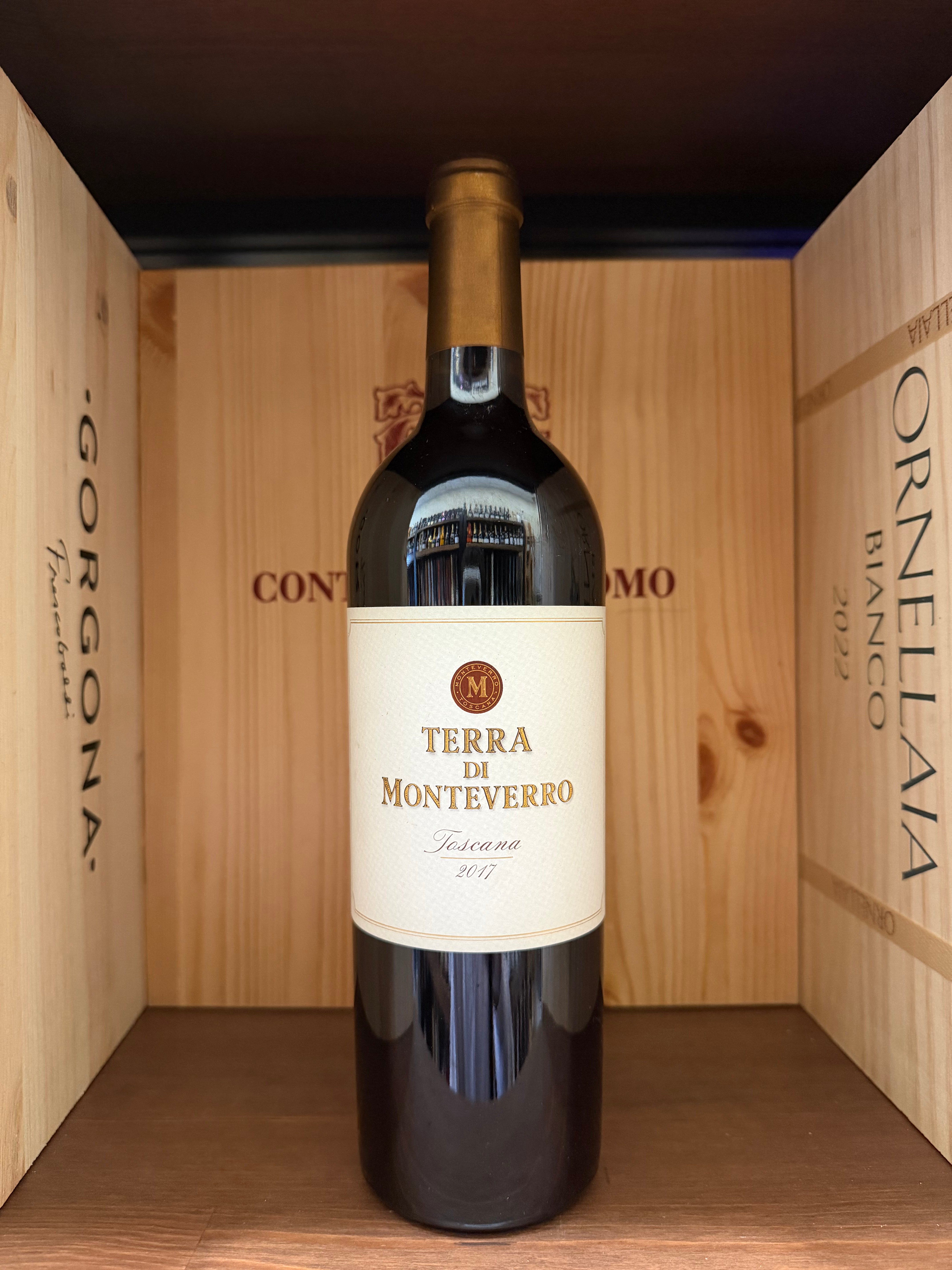 Bottiglia di vino Terra di Montenegro 2017 di Enoteche Toscane, etichetta elegante e dettagliata, in un calice di vino rosso.