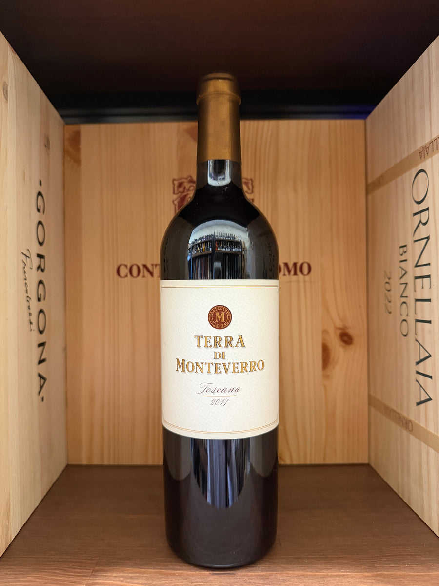 Bottiglia di vino Terra di Montenegro 2017 di Enoteche Toscane, etichetta elegante e dettagliata, in un calice di vino rosso.