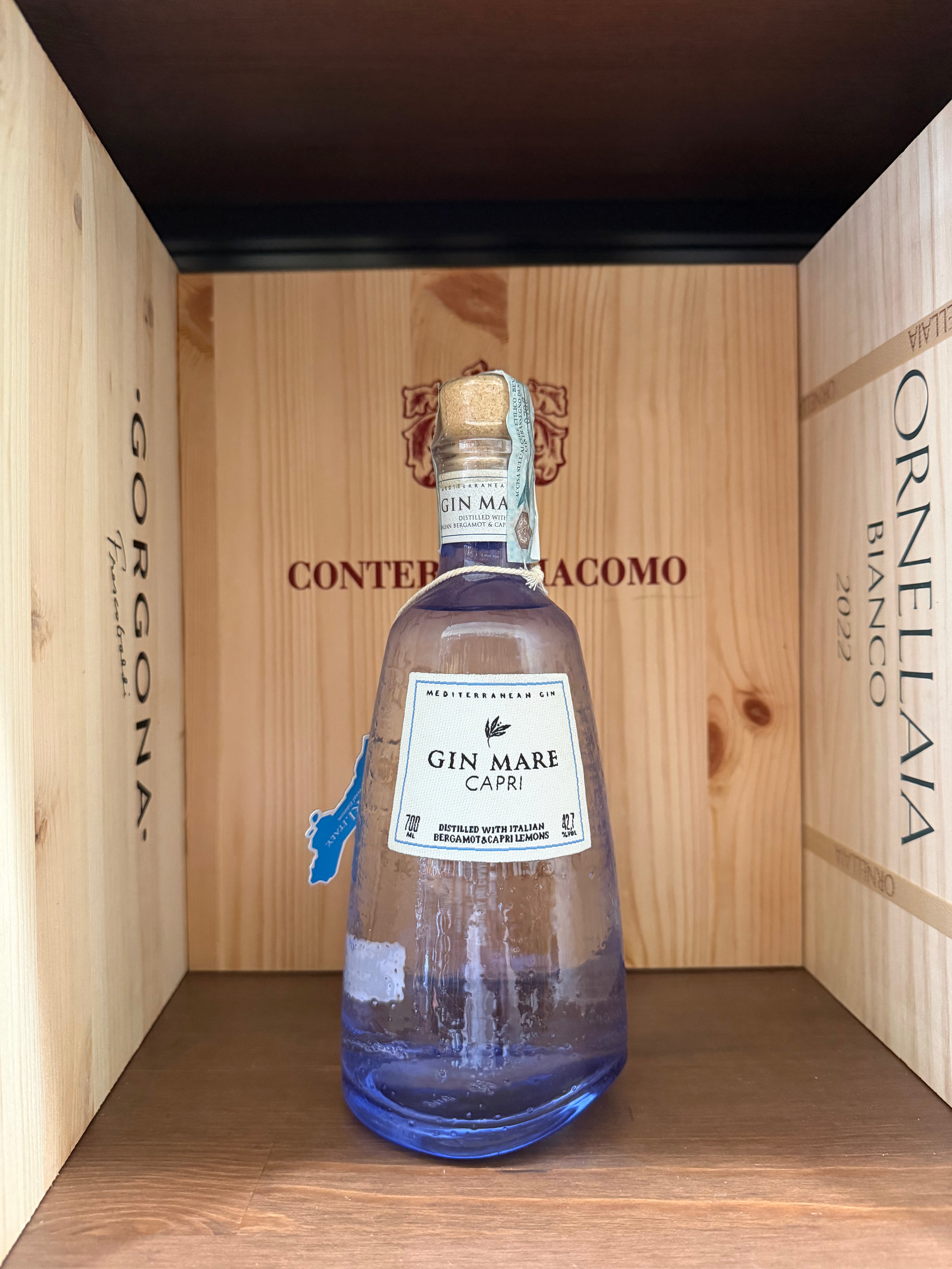 Bottiglia di Gin Mare Capri di Enoteche Toscane, con etichetta elegante e capolino di limoni e piante mediterranee sullo sfondo