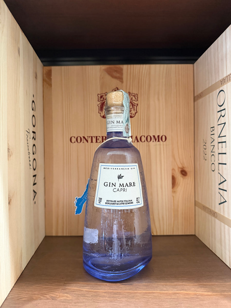 Bottiglia di Gin Mare Capri di Enoteche Toscane, con etichetta elegante e capolino di limoni e piante mediterranee sullo sfondo