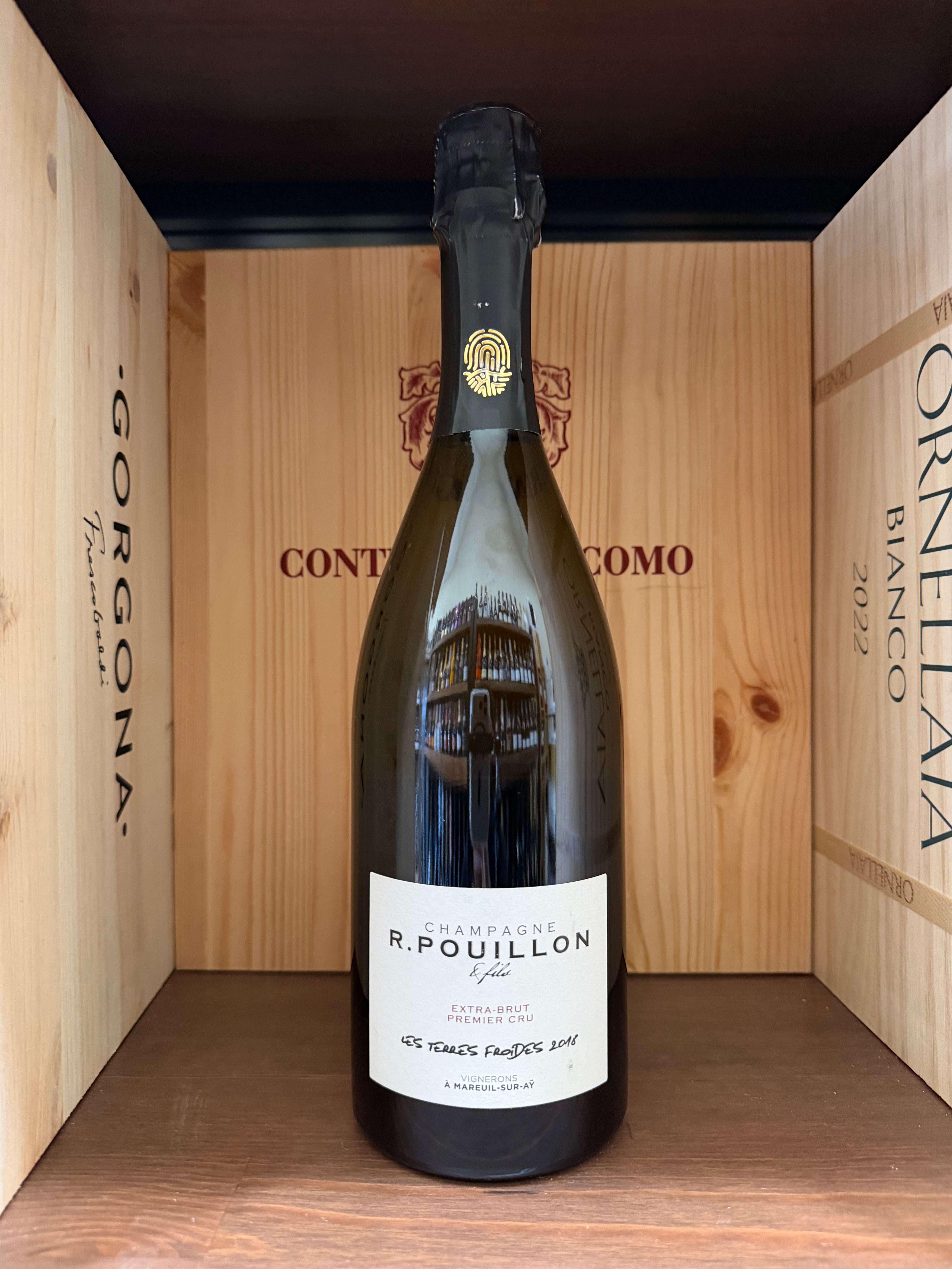 Calice di vino bianco R.Pouillon Les Terres Froides Premier Cru Extra Brut 2018 in un calice, sfondo neutro, dettaglio della bottiglia.