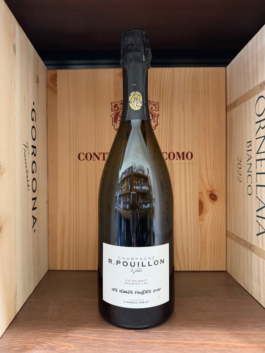 Calice di vino bianco R.Pouillon Les Terres Froides Premier Cru Extra Brut 2018 in un calice, sfondo neutro, dettaglio della bottiglia.