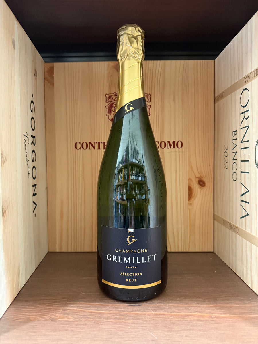 Bottiglia di Gremillet Sèlection Brut, champagne italiano con etichetta elegante, in un bicchiere e sfondo neutro.